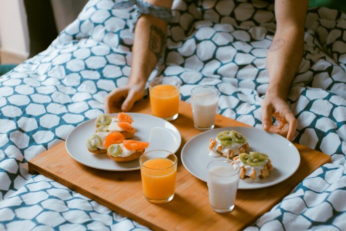 Photo by Toa Heftiba person serving pastries on white ceramic plates with fruit juice glasses on wooden tray on top of bed