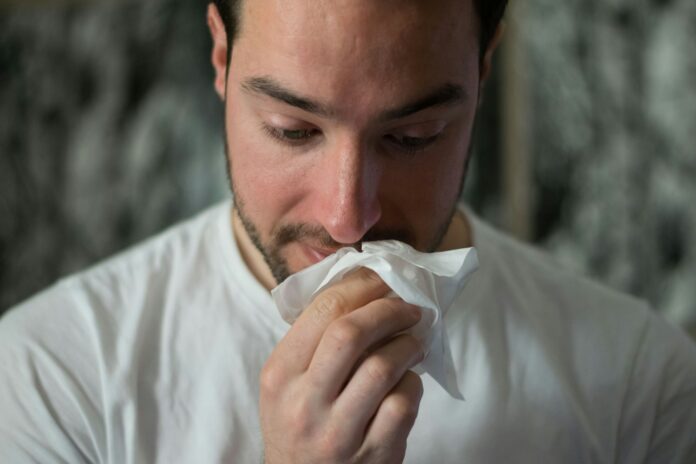Photo by Brittany Colette sick man blowing nose into tissue
